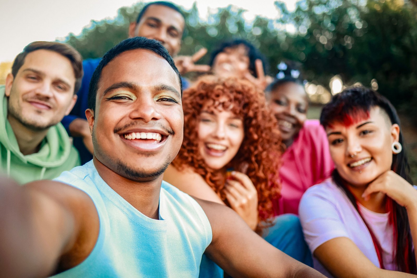 Young diverse people smiling at mobile phone camera at city park. African nonbinary taking selfie with friends. LGBT community