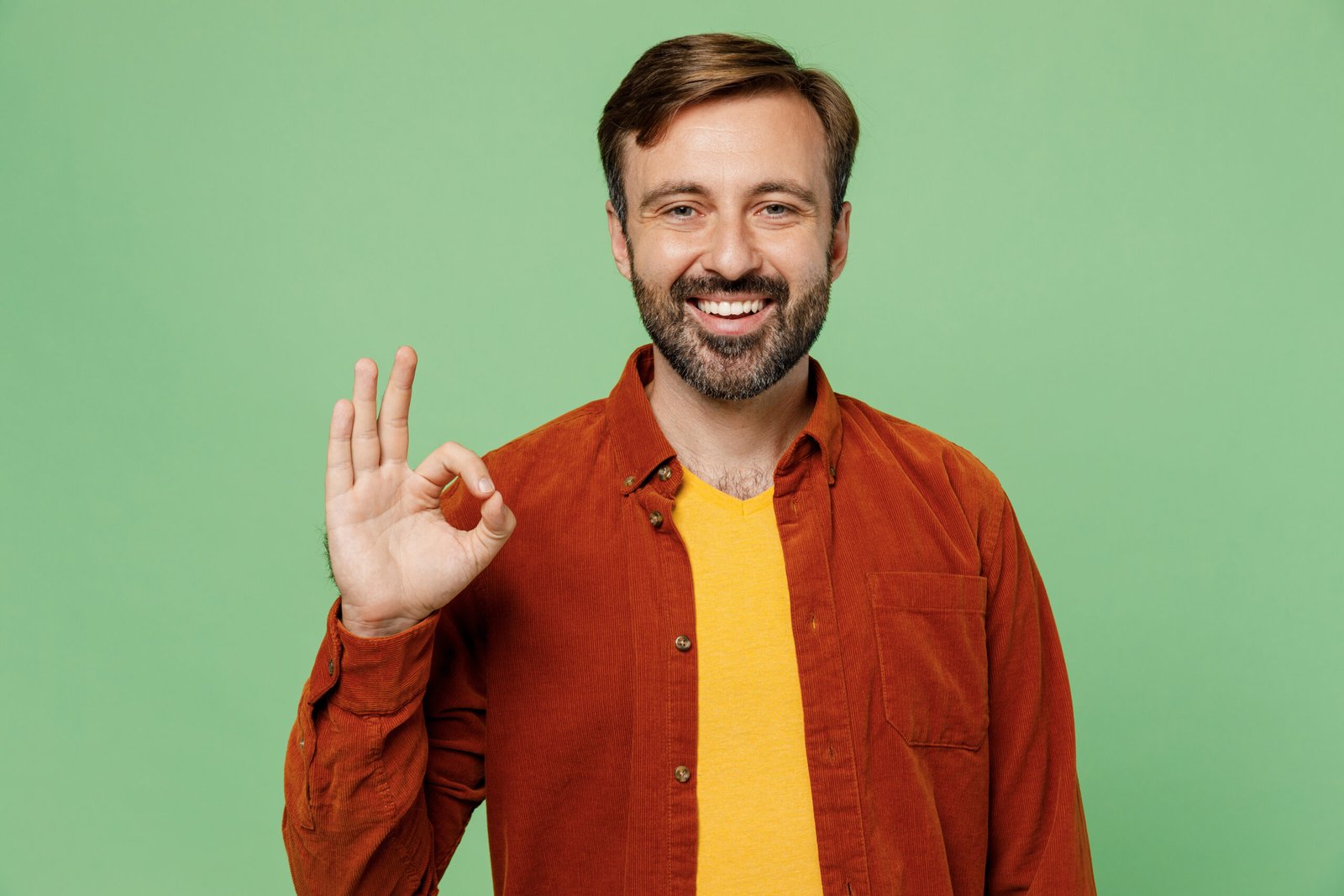 Elderly smiling happy fun satisfied positive caucasian man 40s years old wears casual clothes red shirt t-shirt showing okay ok gesture isolated on plain pastel light green background studio portrait.