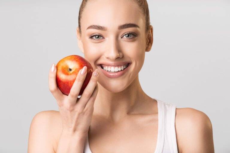 Woman With Perfect Smile Holding Apple Posing On Gray Background